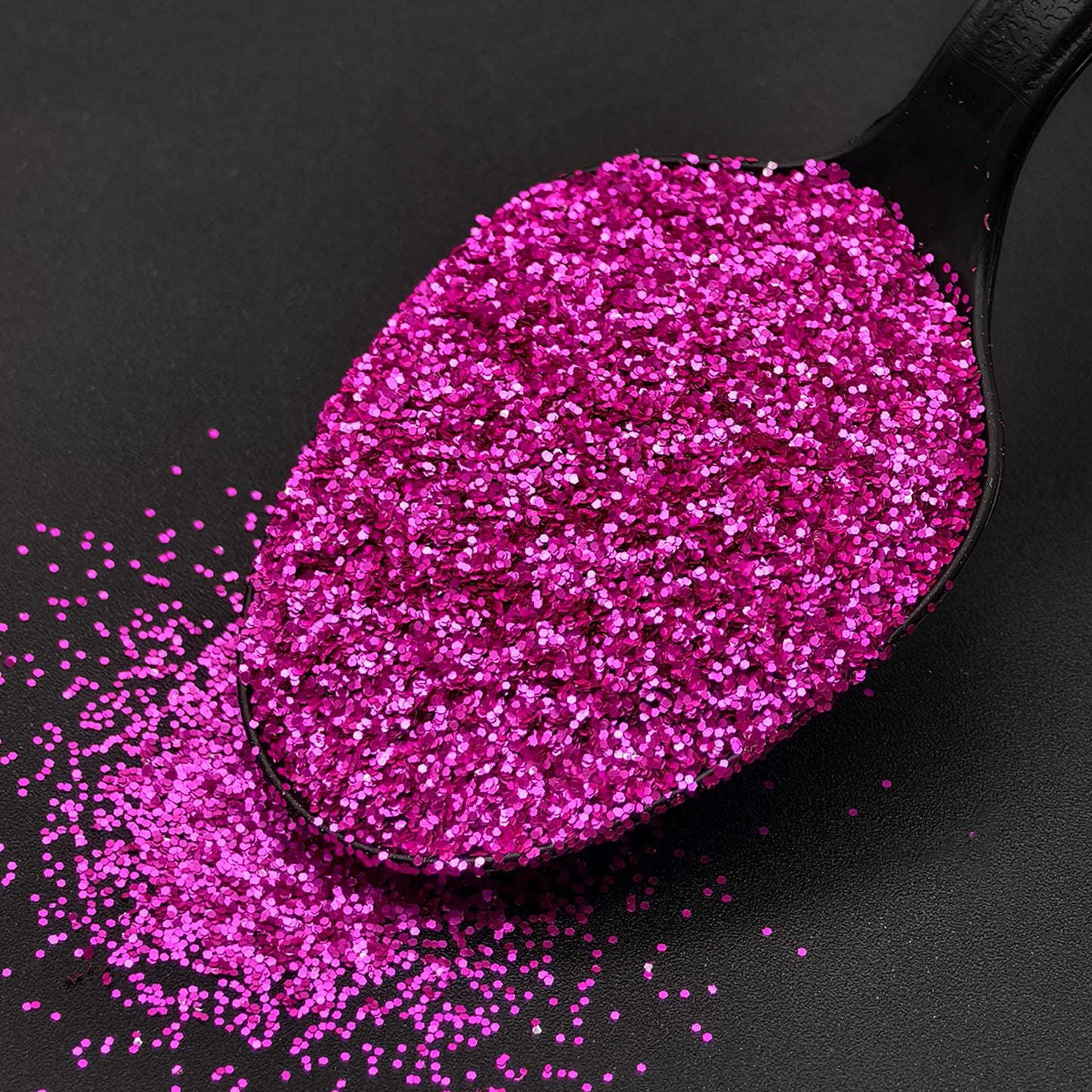 Black spoon filled with pink glitter on a black background