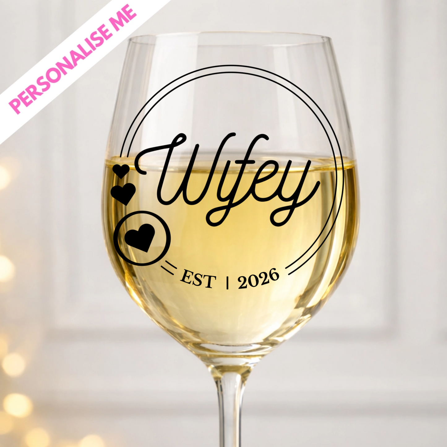 Wine glass with 'Wifey' and 'EST 2026' text, filled with white wine, on a light background.