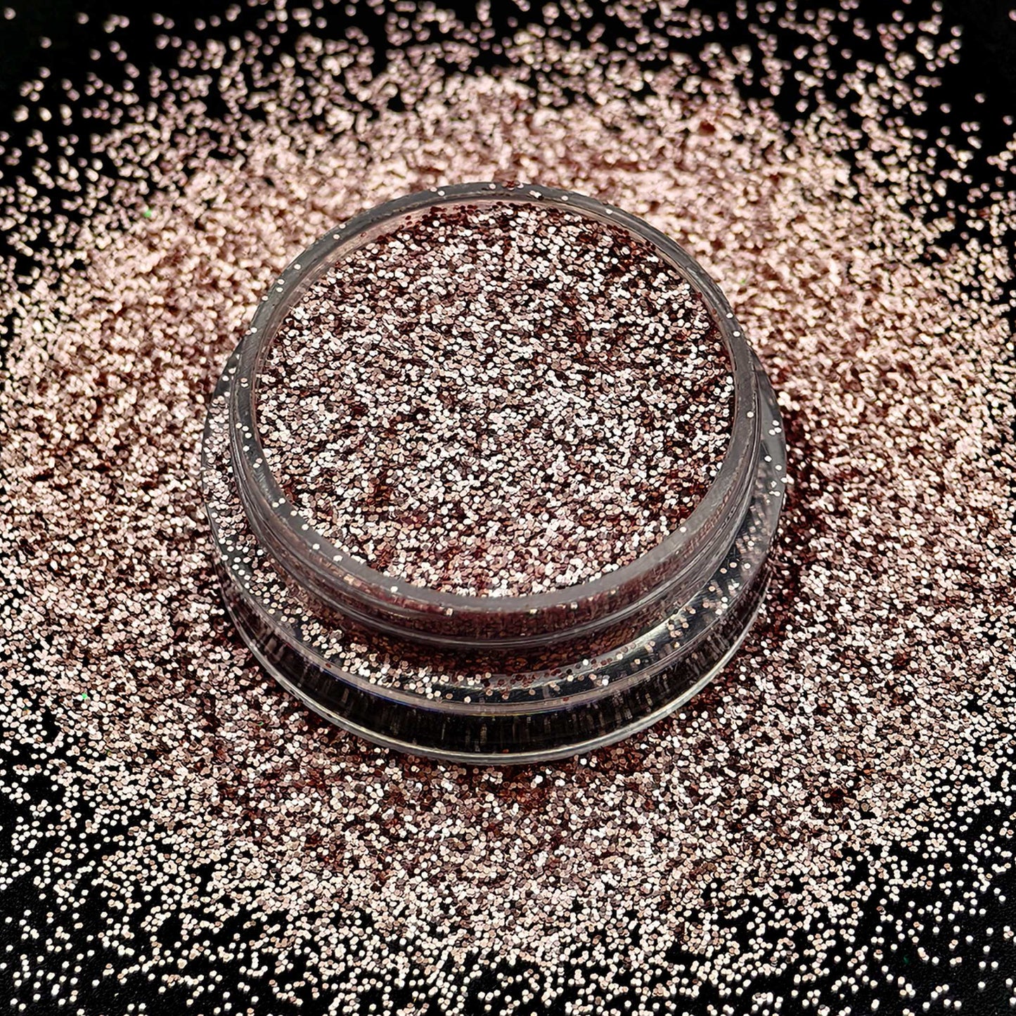 Rose gold glitter in a small container on a black background