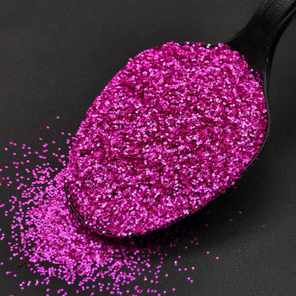 Black spoon filled with pink glitter on a black background