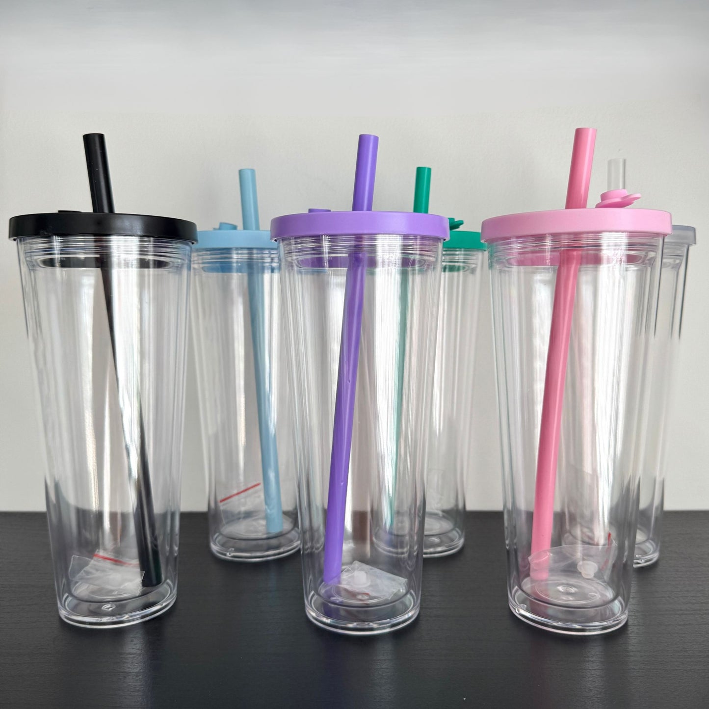 Set of clear tumblers with colorful lids and straws on a black surface.