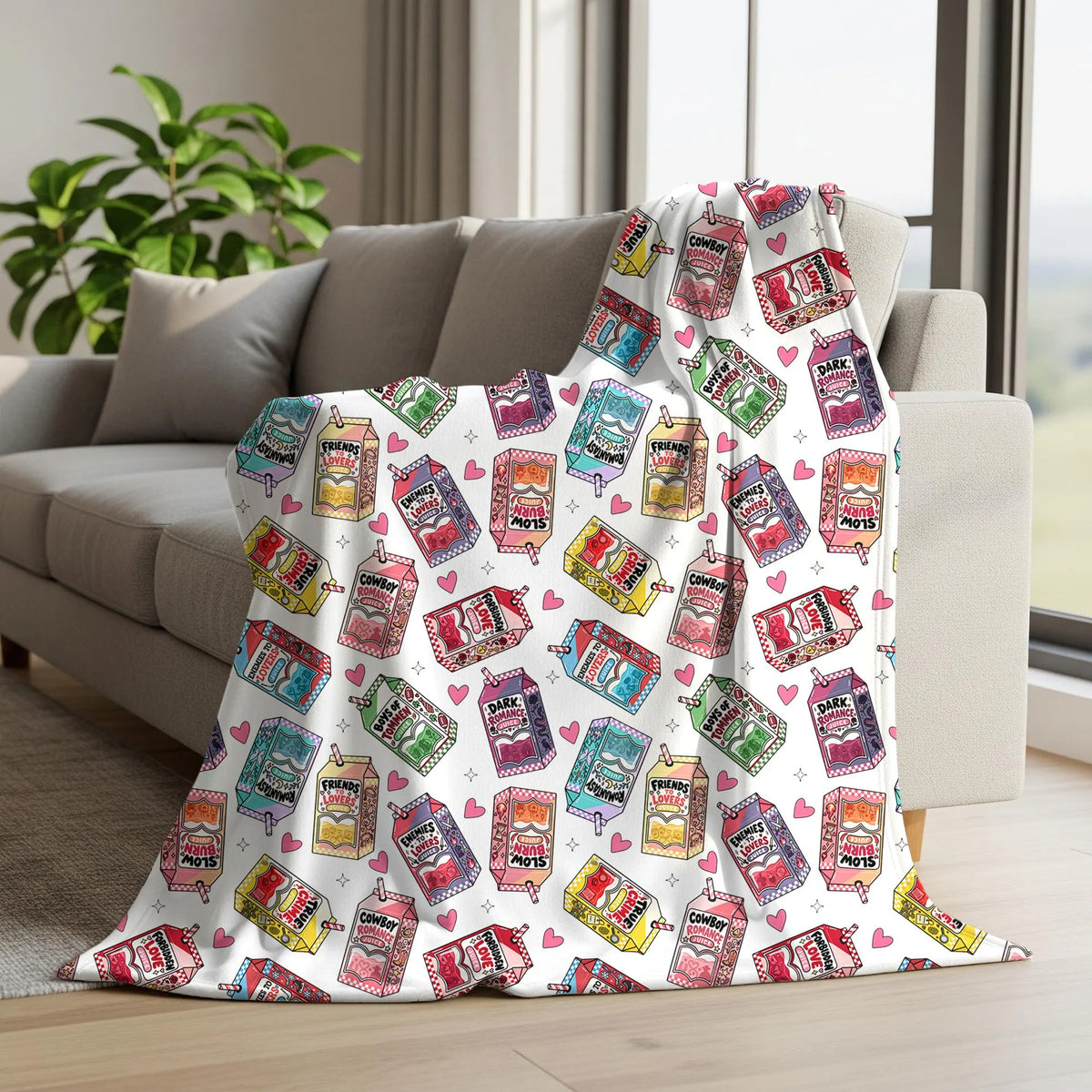 Bookish romance tropes seamless pattern printed on a throw blanket with colourful romance genre juice cartons and pink hearts.