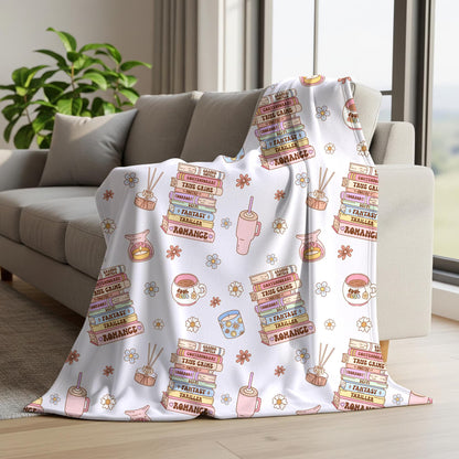 Cosy book lover seamless pattern displayed on a blanket with pastel book stacks, pink drinks, reading accessories and delicate floral illustrations.
