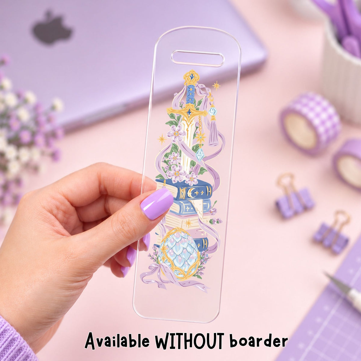 A hand with lavender nail polish holds a clear phone case featuring a detailed illustration of a fantasy book tower with purple ribbons, flowers, and gold accents. The background is a soft pink desk with purple-themed stationery, including a laptop, washi tape, and binder clips.