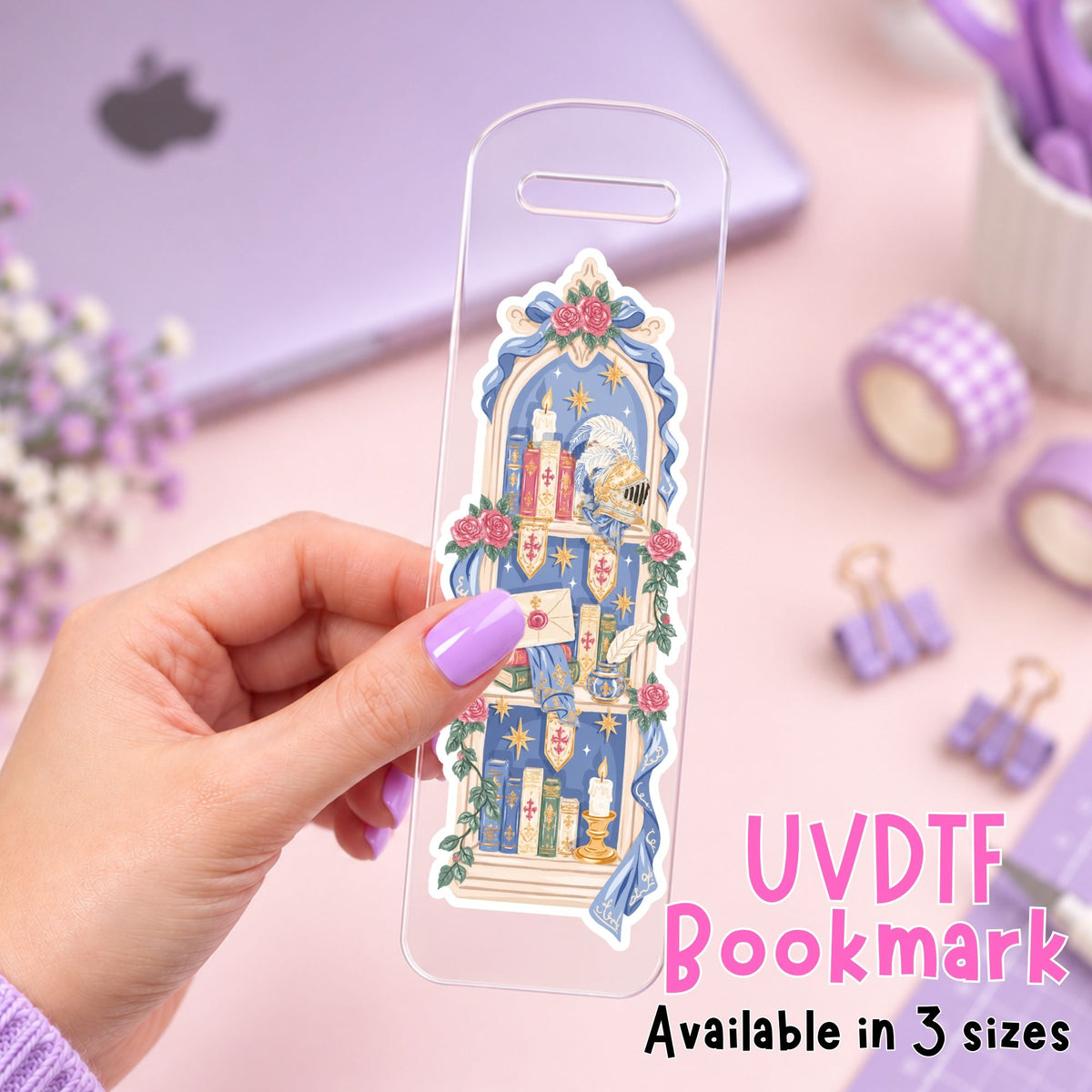 A hand with lavender nail polish holds a clear acrylic bookmark featuring a whimsical illustration of a mouse in a blue coat and hat, surrounded by pink roses and candles. The image is set against a pastel pink desk background with a laptop, washi tape, and binder clips, with text overlay reading 'UVDTF Bookmark Available in 3 sizes'.