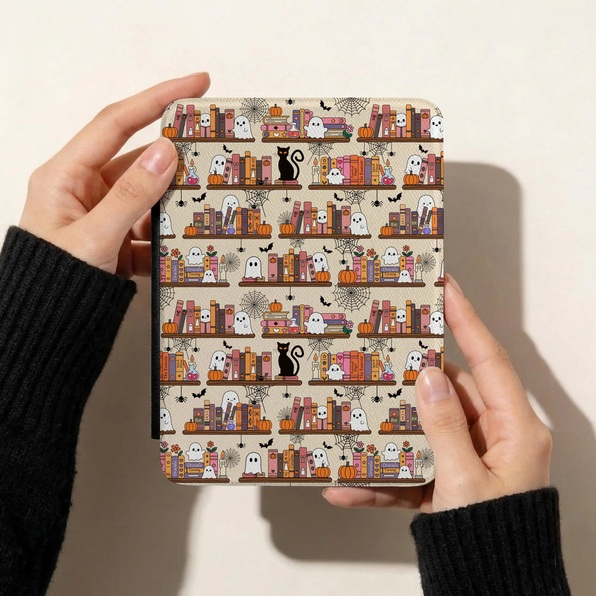 Spooky Halloween bookshelf seamless pattern on a Kindle cover featuring cute ghosts, pumpkins, black cats, colourful books and spiderwebs.
