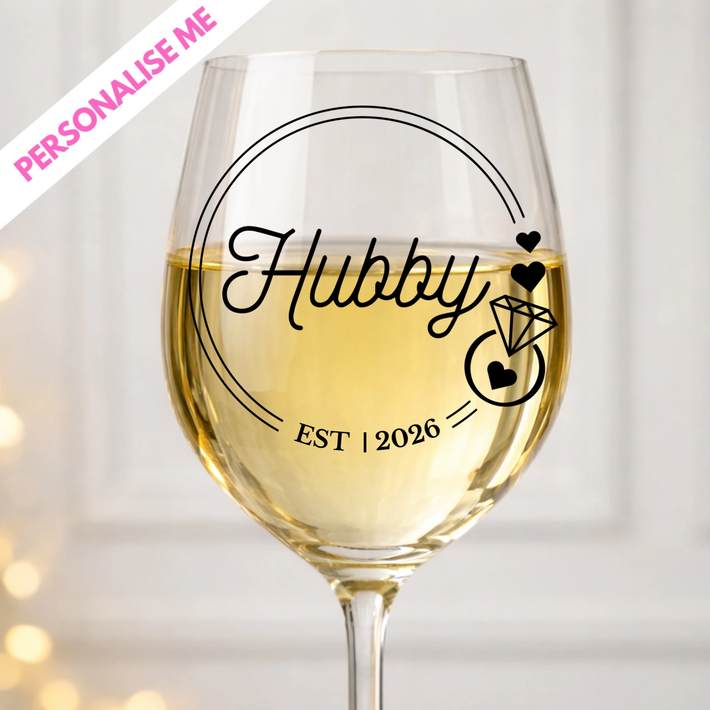 Wine glass with 'Hubby' and 'EST 2026' text, filled with white wine, on a blurred background.
