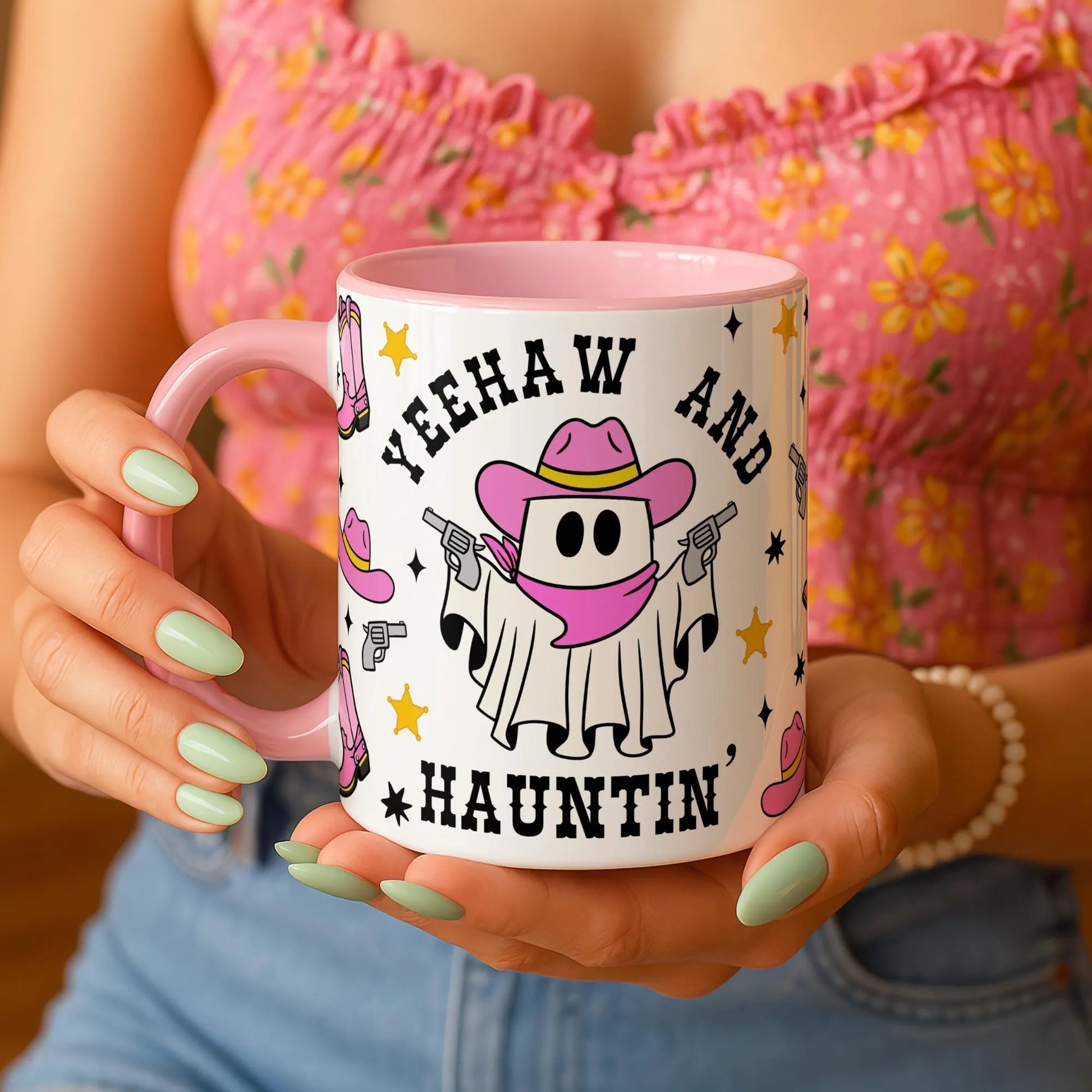 Person holding a mug with a cartoon ghost in a cowboy hat and boots design, text 'YEEHAW AND HAUTIN', and pink handle.