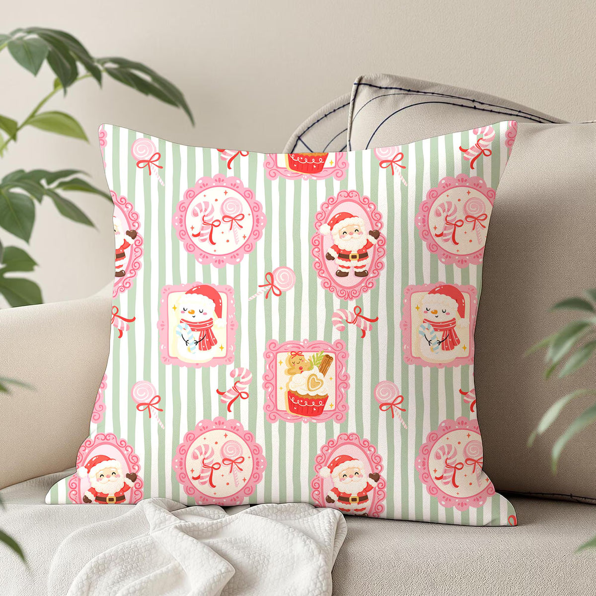 A square decorative throw pillow with a festive Christmas pattern, styled on a beige sofa with a white blanket and green plant leaves in the background.