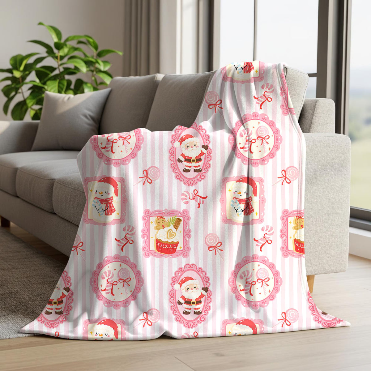 A white throw blanket with pink vertical stripes and festive Christmas motifs, draped over a gray sofa in a bright living room.